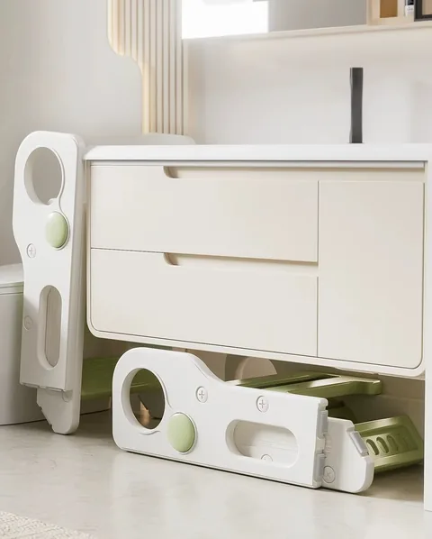 Dos banquitos verdes plegados, uno apoyado a la par del inodoro y otro guardado debajo del mueble del baño