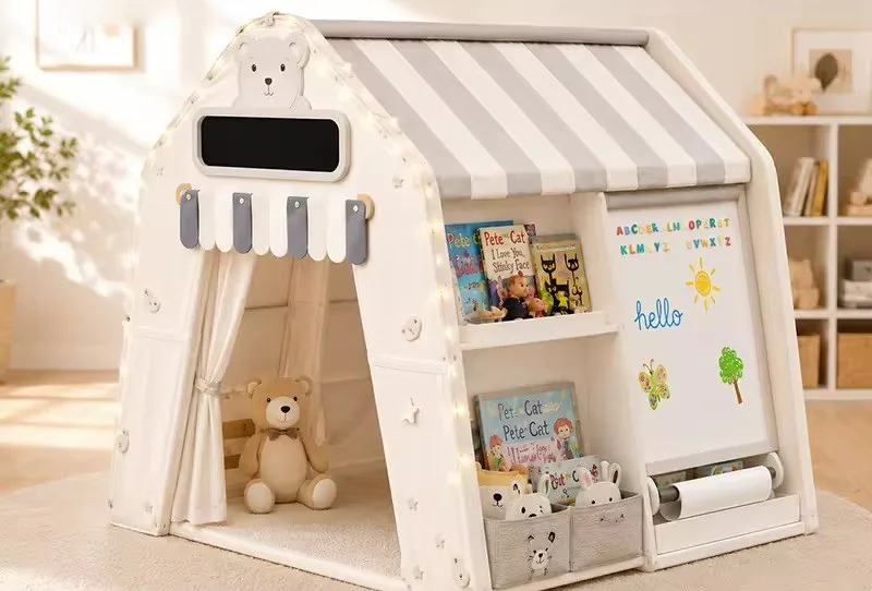 Casita de juego con estante de cuentos, canastas, pizarra blanca con rollo de papel y un oso de peluche en la entrada