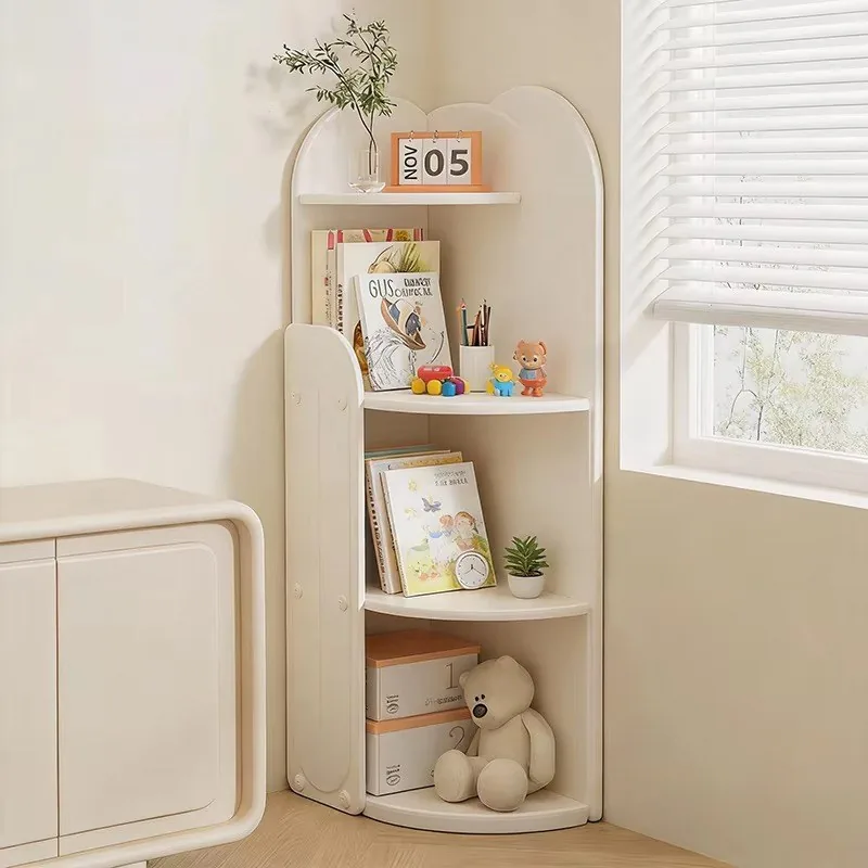 Estante esquinero blanco crema de cuatro niveles con cuentos, peluches y un calendario, colocado en la esquina de un cuarto