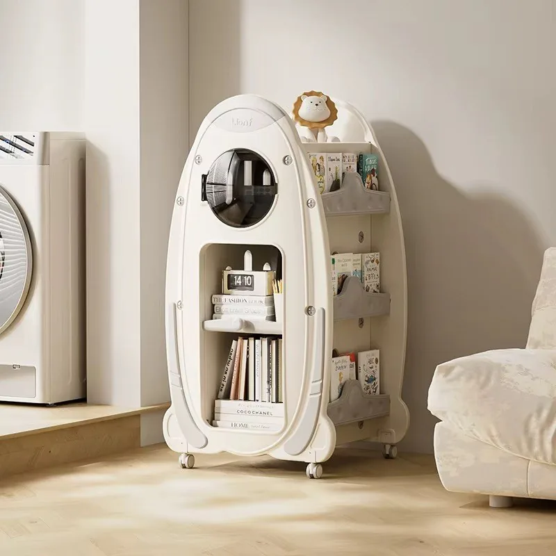 Librero en forma de cohete blanco crema con bolsillos grises, ventana redonda, repisa abierta y un leoncito arriba, junto a un sillón