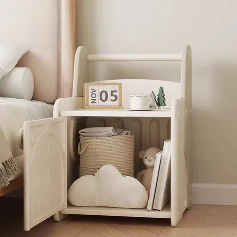 Mesita de noche con la puerta abierta y el gabinete lleno con un canasto, un cojín de nube, un peluche y libros