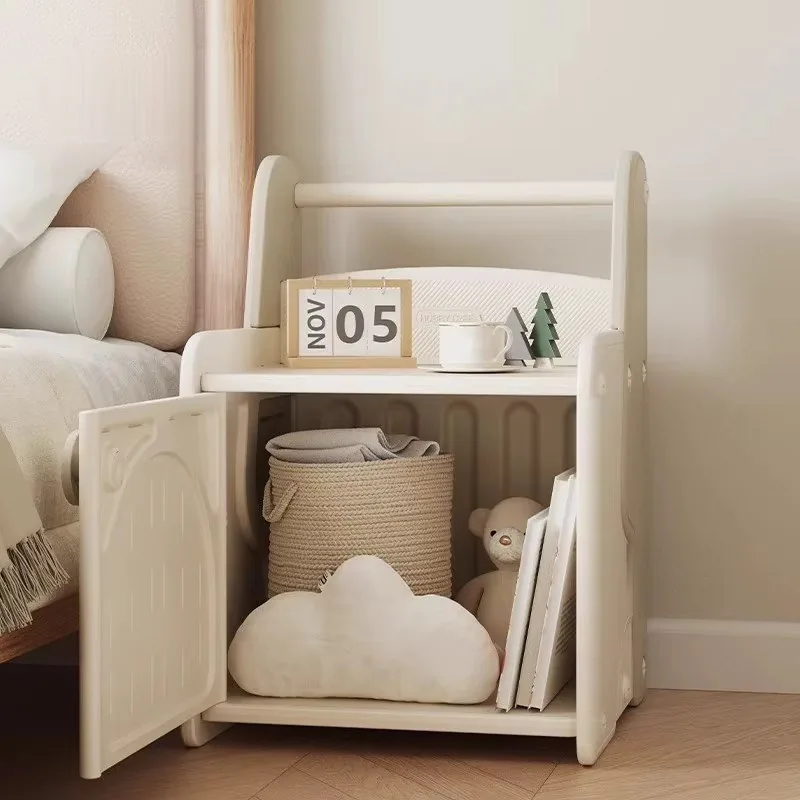 Mesita de noche con la puerta abierta y el gabinete lleno con un canasto, un cojín de nube, un peluche y libros