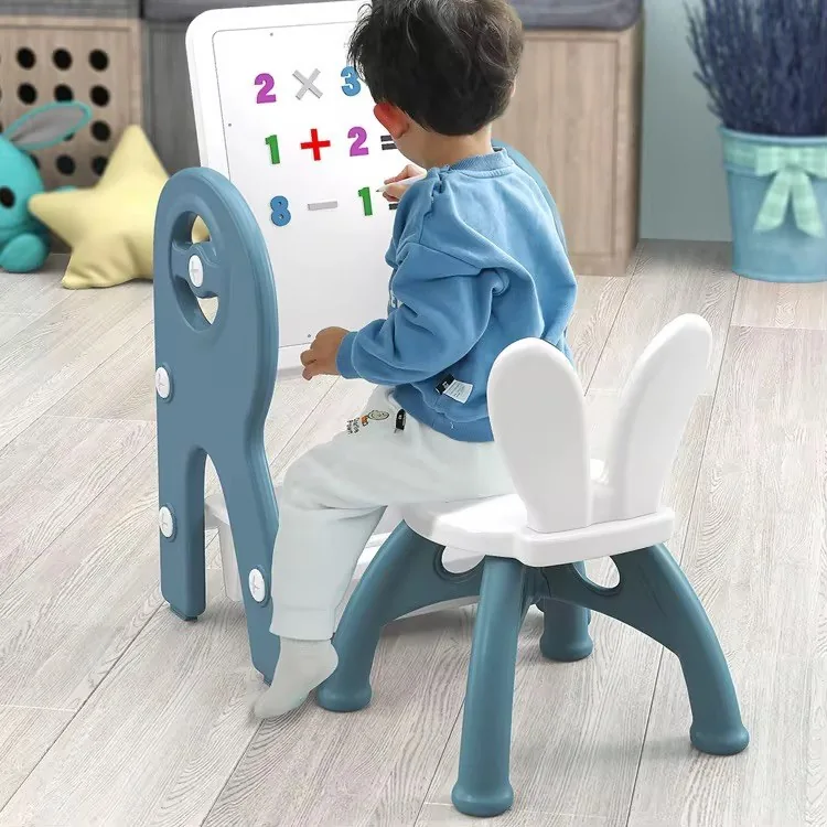 Niño sentado en la silla con orejas de conejo escribiendo números en la pizarra levantada de la mesa