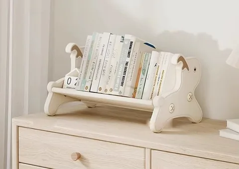 Librerito de mesa lleno de cuentos sobre un mueble de madera clara, junto a una cortina