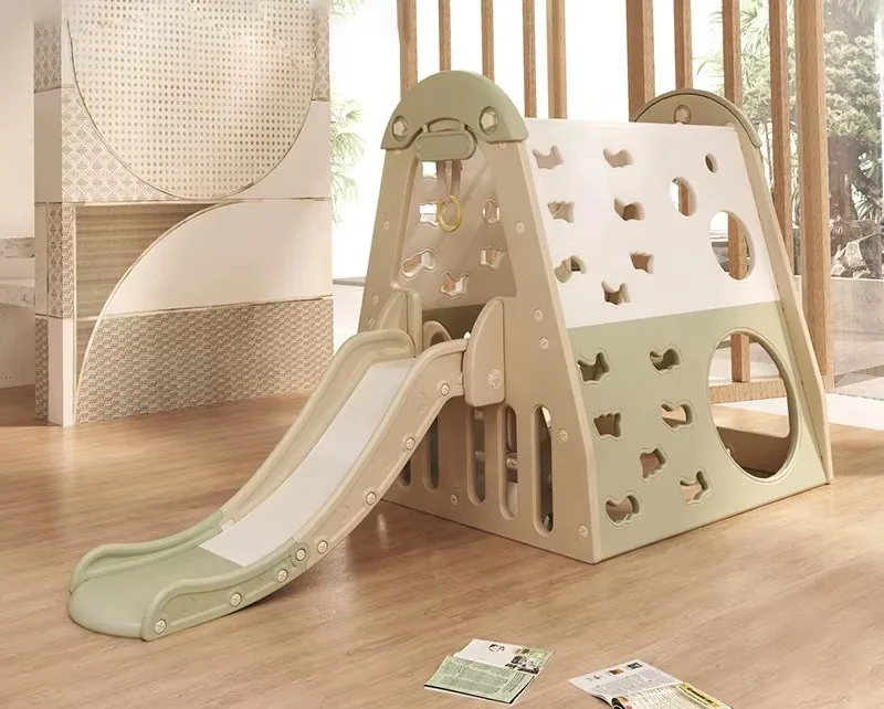 Play en forma de casita con pared de escalar, túnel redondo y tobogán verde salvia, en una sala con piso de madera
