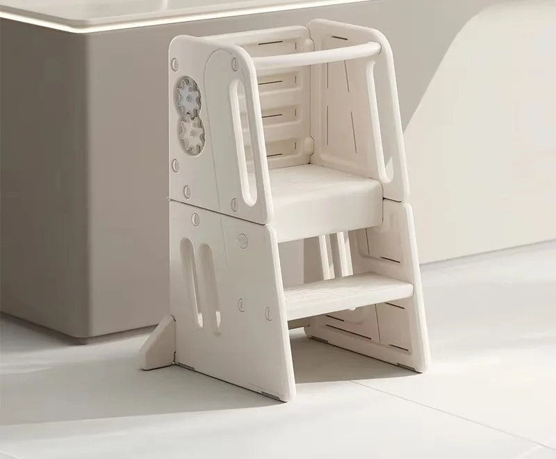 Torre de aprendizaje blanca crema con dos escalones y plataforma con baranda, junto a una isla de cocina