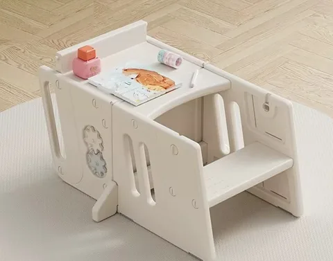 Torre de aprendizaje separada en dos piezas y armada como mesa con asiento, con un libro y juguetes encima